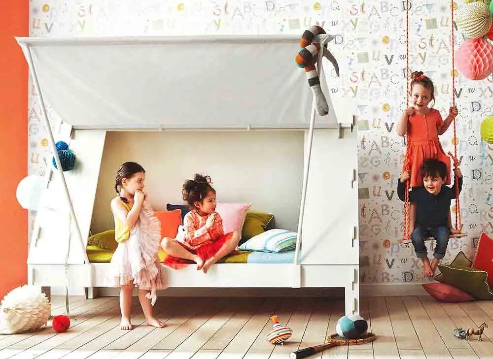 Cama infantil branca com almofadas coloridas e crianças a brincar com balanço em quarto decorado.