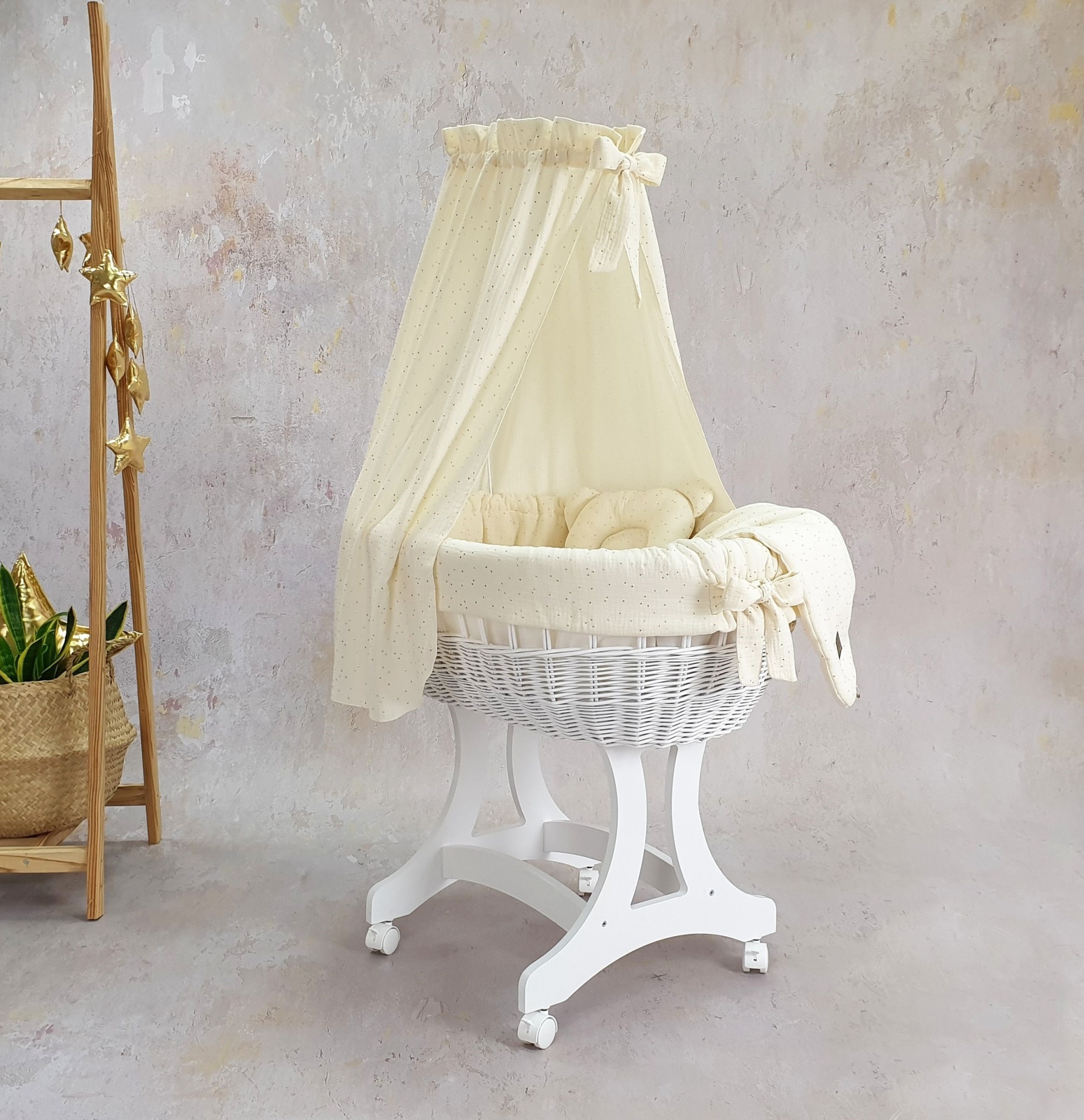 Cesta Moisés de Vime Branco EMMA com Roupa de Cama Berço de bebé redondo em vime branco com dossel amarelo pálido, sobre suporte de madeira e rodas, em ambiente neutro