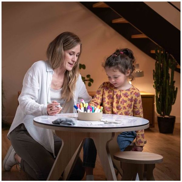 Base de Mesa para Desenhar Dupla Face Mulher e criança a desenhar numa mesa redonda branca com canetas coloridas, ambiente interior com planta.