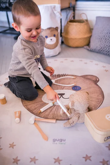 Tapete Redondo Borracha Natural URSO TEDDY Criança brinca num tapete redondo com padrão de urso e brinquedos de madeira