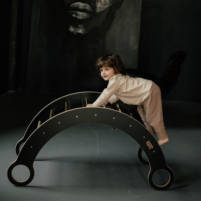 Balanço de Madeira MONTESSORI Criança a brincar numa estrutura de madeira curva preta