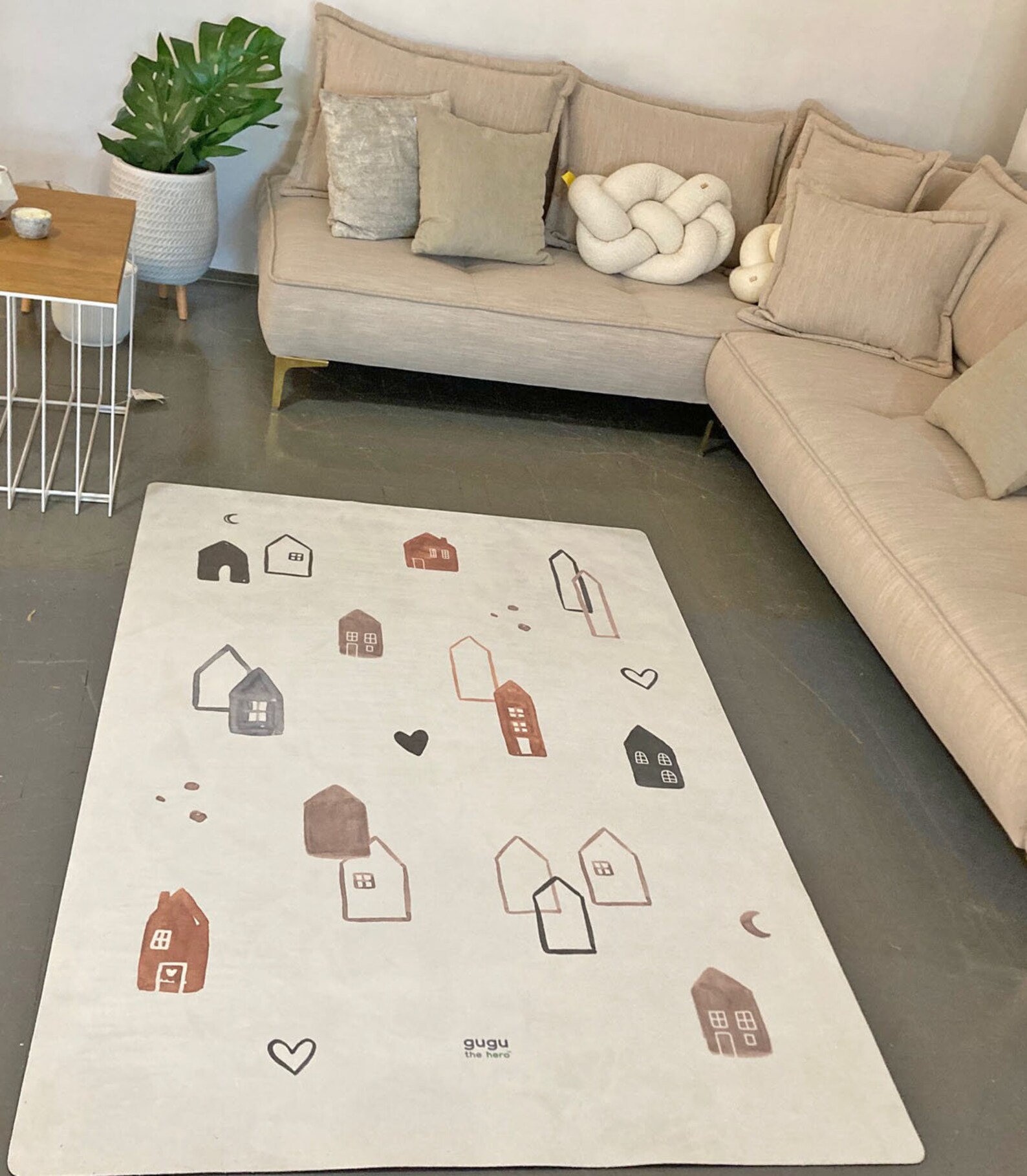 Tapete Retangular Ecológico CIDADE ESCANDINAVA Tapete branco com desenhos de casas coloridas junto a sofá bege e mesa lateral de madeira