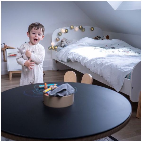 Base de Mesa para Desenhar Dupla Face Quarto infantil com cama branca, mesa preta redonda e menino a brincar