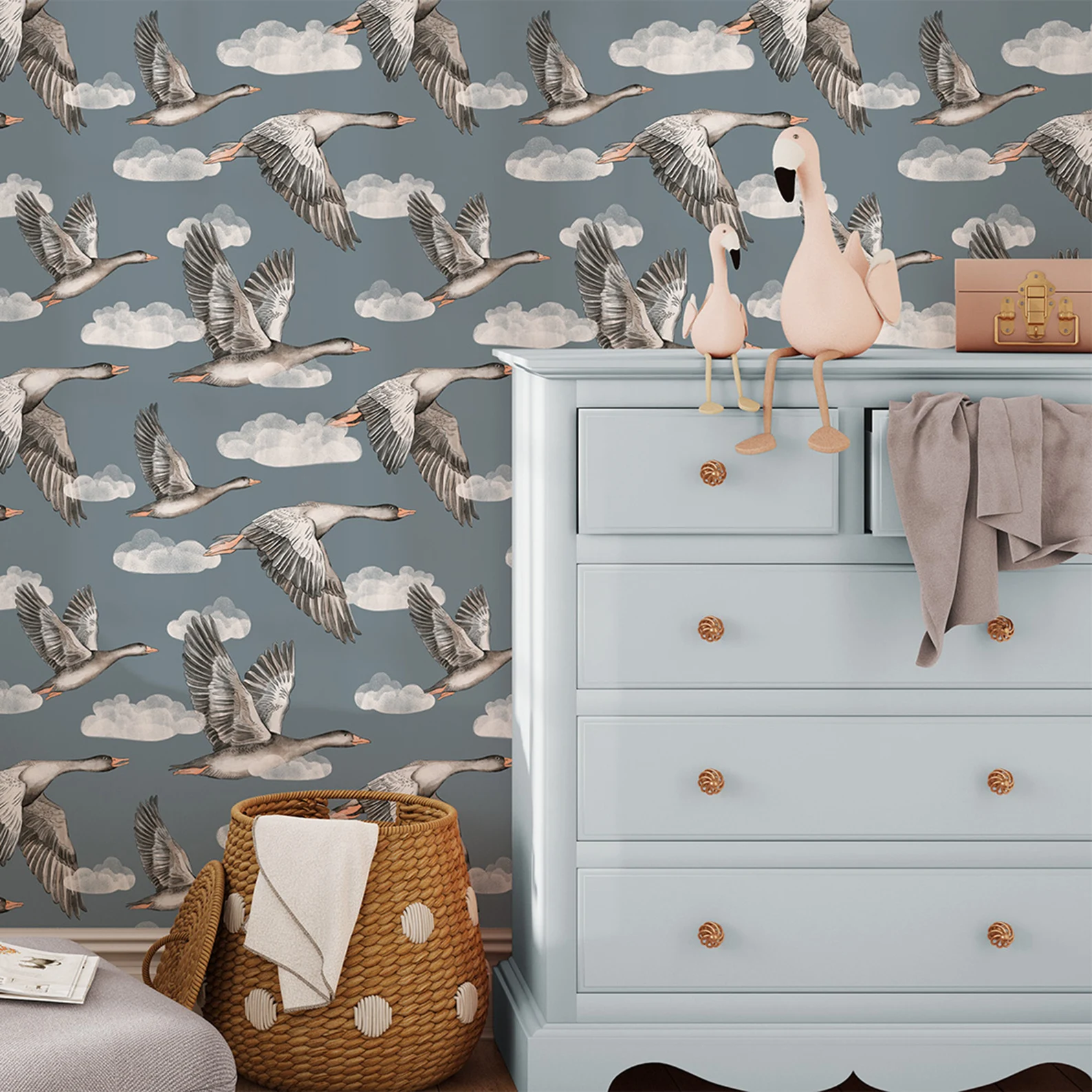 Papel de Parede Infantil Gansos Azuis Papel de parede com gansos em voo azul cinzento e cômoda azul claro com peluches de aves cor-de-rosa e cesta de vime.