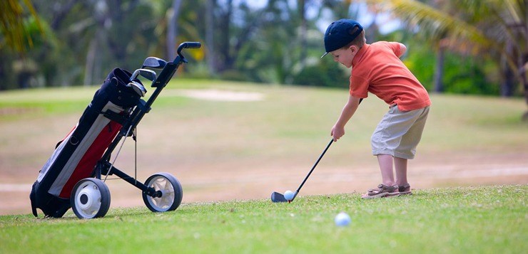 Criança a jogar golfe num campo verde com carrinho de golfe ao lado