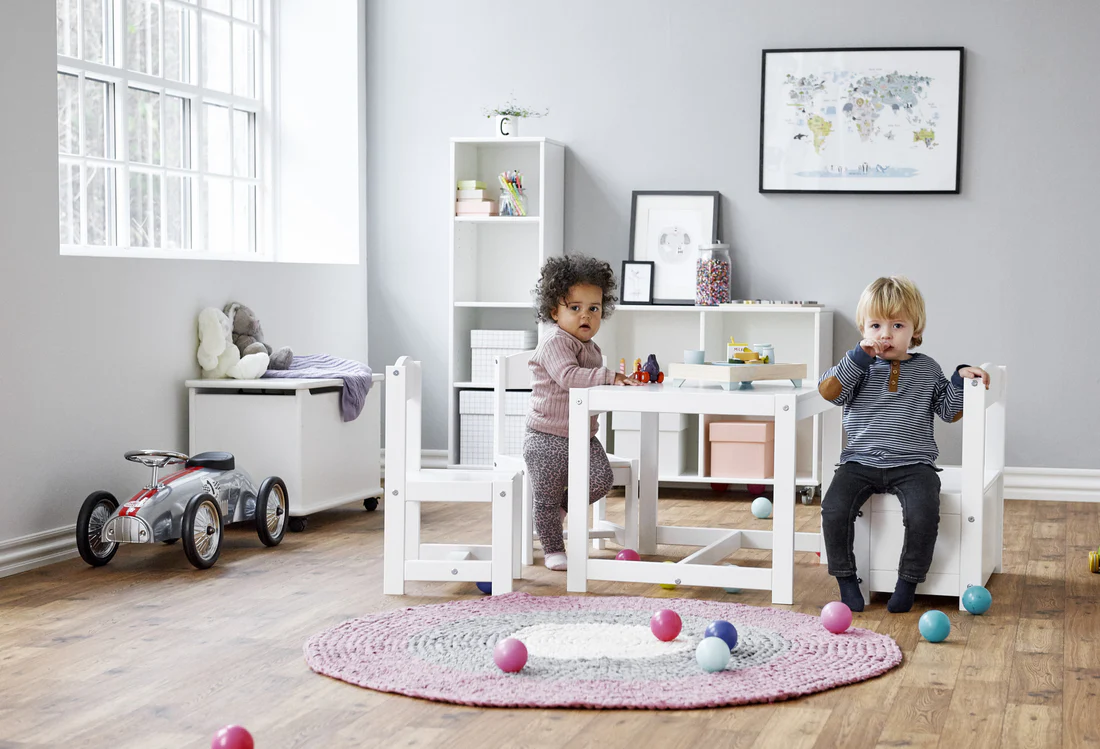 Conjunto Infantil MATILDE – Mesa, Cadeiras e Banco com Arrumação Quarto infantil com mesa e cadeiras brancas, tapete rosa e crianças brincando