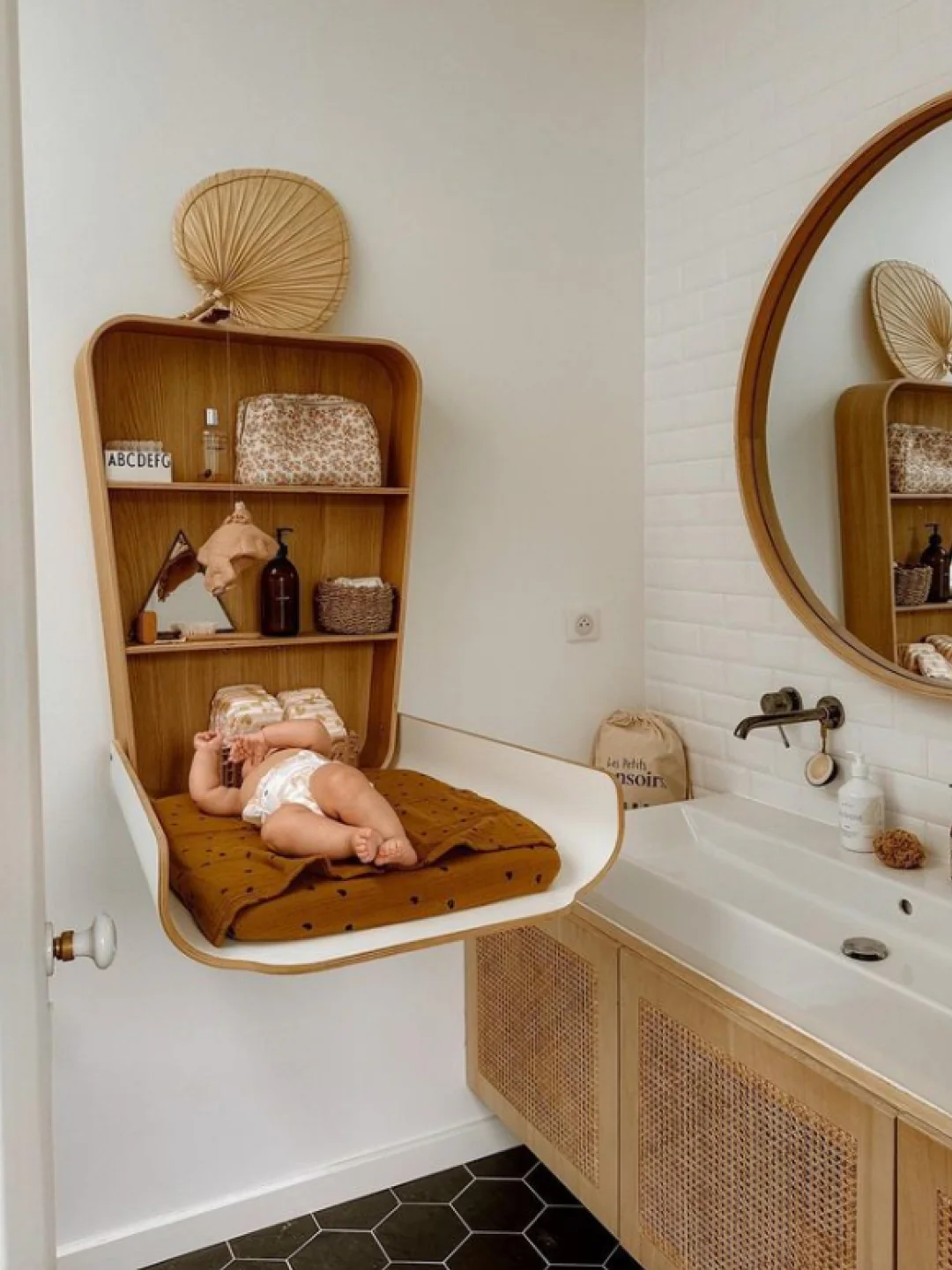 Trocador de Fraldas NOGA para Parede Cama suspensa para bebé com almofada castanha em quarto branco e lavatório com armário em madeira grelha