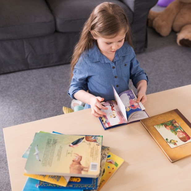 Criança a ler livro infantil numa mesa com livros coloridos