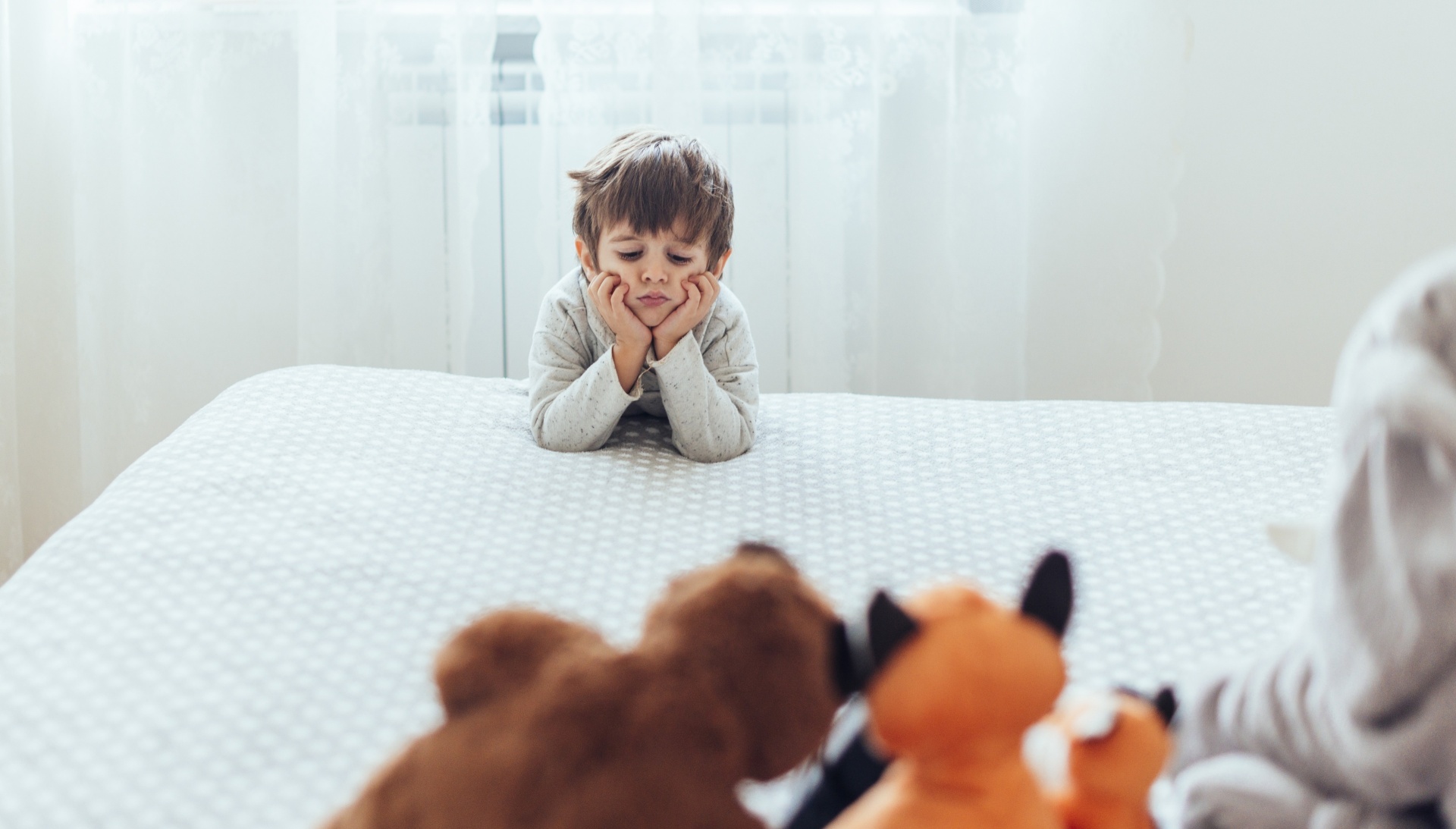 Transformar a Hora de Dormir em Momentos de Confiança! Criança deitada numa cama a olhar para peluches