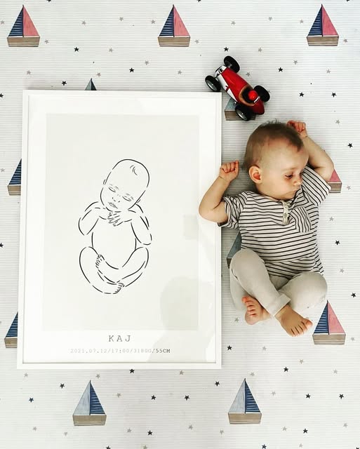 Tapete Ecológico PEQUENO MARINHEIRO Pôster de desenho de bebé em moldura branca junto a bebé real adormecido sobre lençol decorado com barcos e estrelas