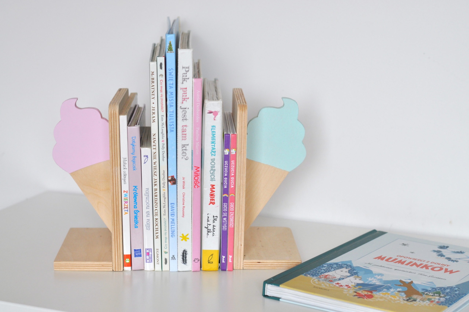 Conjunto Suporte para Livros GELADO Suporte de livros em madeira decorado com gelados e livros infantis variados numa mesa branca.