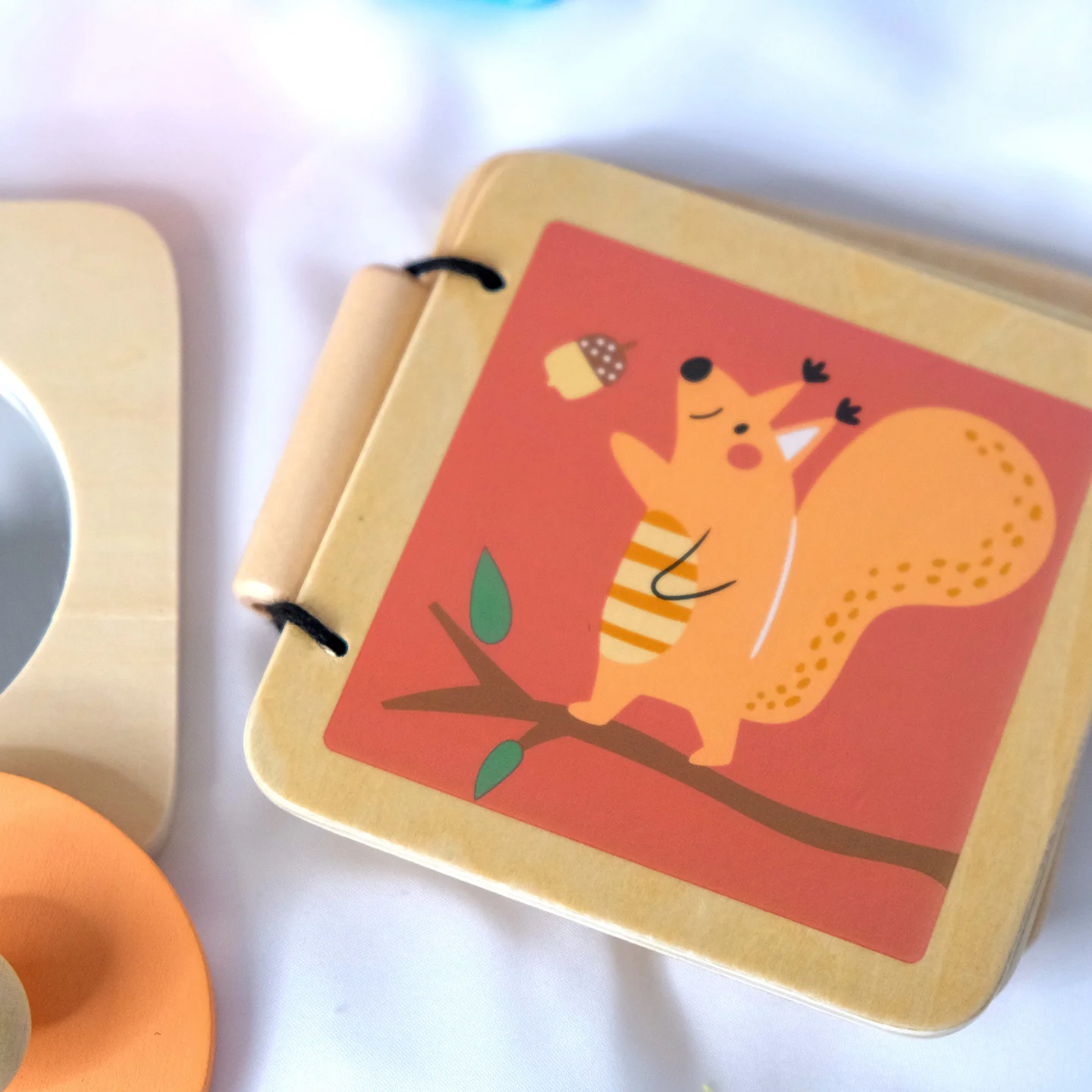 Caixa Sensorial Montessori - 6 a 12 meses Livro infantil de madeira com ilustração de esquilo laranja segurando bolota.