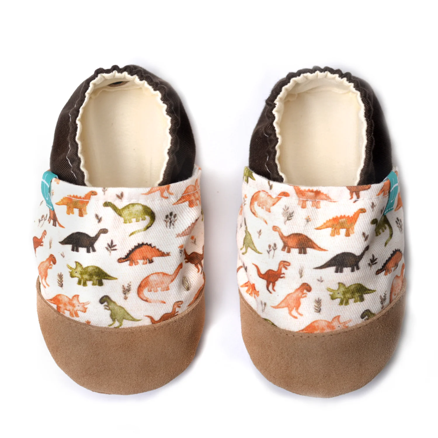 Sapatinhos de Criança em Couro Natural – Dinossauro Marron Chinelos de criança com estampado de dinossauros coloridos e biqueira em camurça castanha.