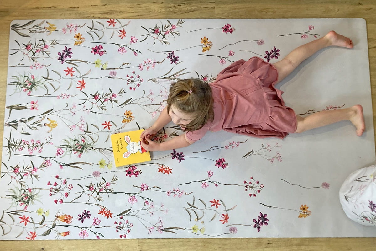 Tapete Grande ECO Jardim de Flores Criança deitada em tapete floral segurando livro amarelo