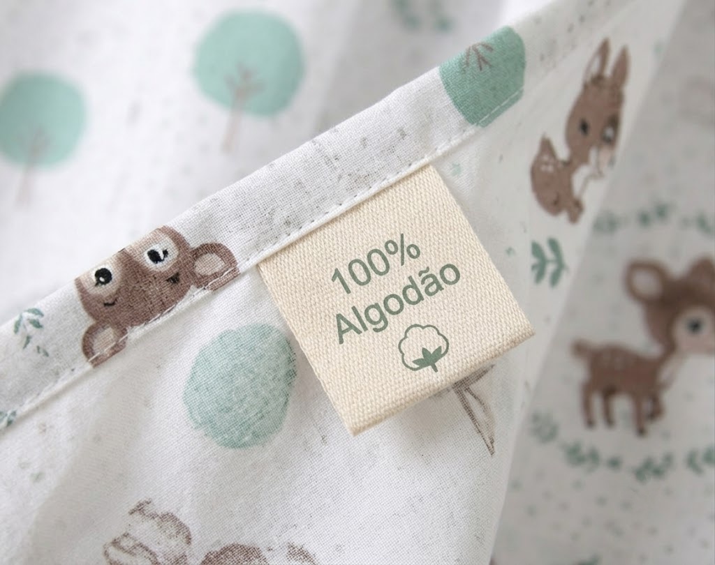 Cortinados Infantis Veadinho da Floresta Etiqueta de tecido com texto 100% Algodão em tecido branco com desenhos de animais e árvores.