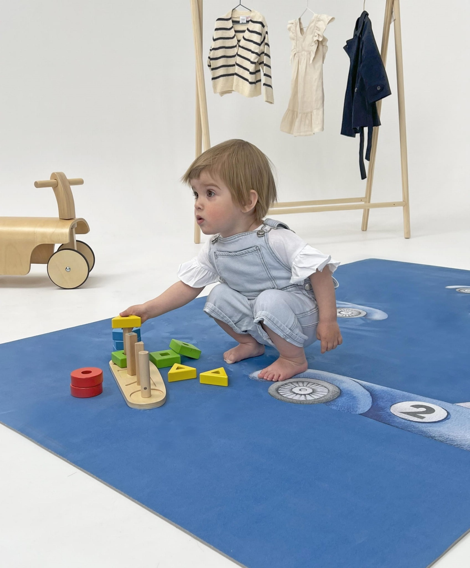 Tapete Educativo ECO Carros de Corrida PRIME Criança a brincar com brinquedo de madeira colorido num tapete azul com rodas numeradas