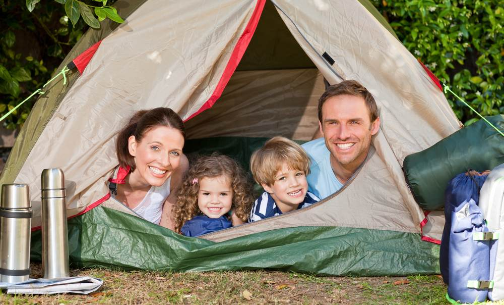 Família sorridente na entrada de tenda de campismo rodeada por natureza