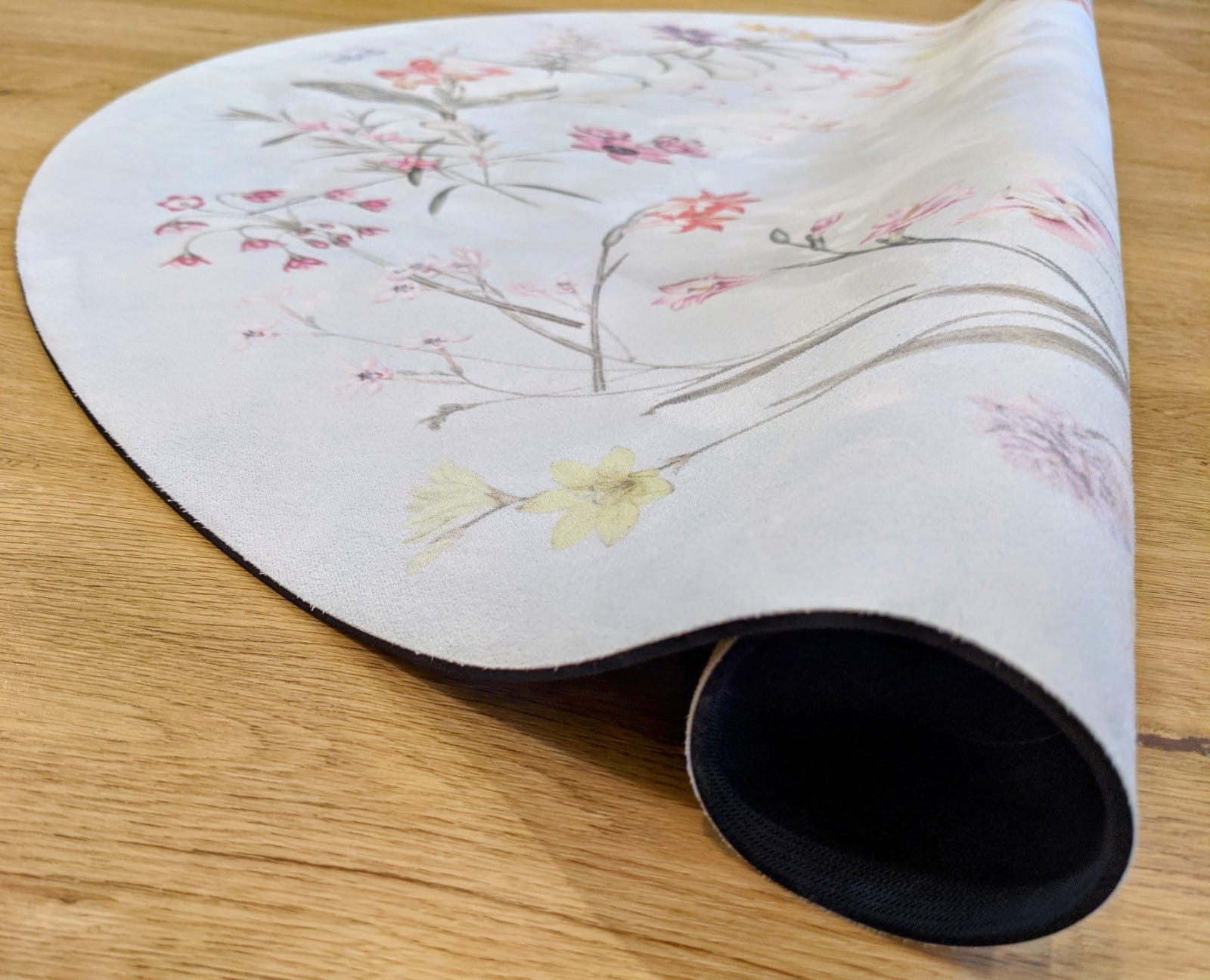 Tapete Redondo ECO de Bebé Jardim de Flores Tapete branco com padrão floral pastel e base preta sobre superfície de madeira