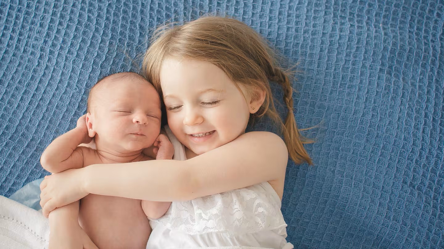 Criança abraçando recém-nascido deitado sobre manta azul