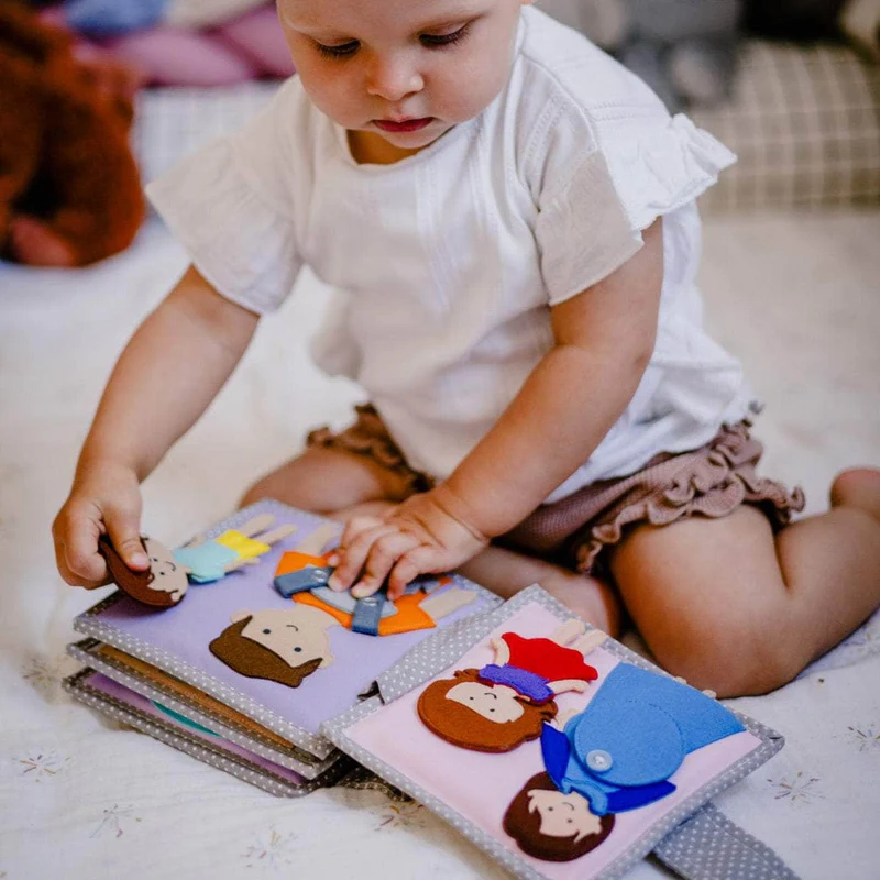 Bebé Feliz – MINI Livro Sensorial de 6 Páginas Criança a brincar com livro de tecido colorido e figuras destacáveis.