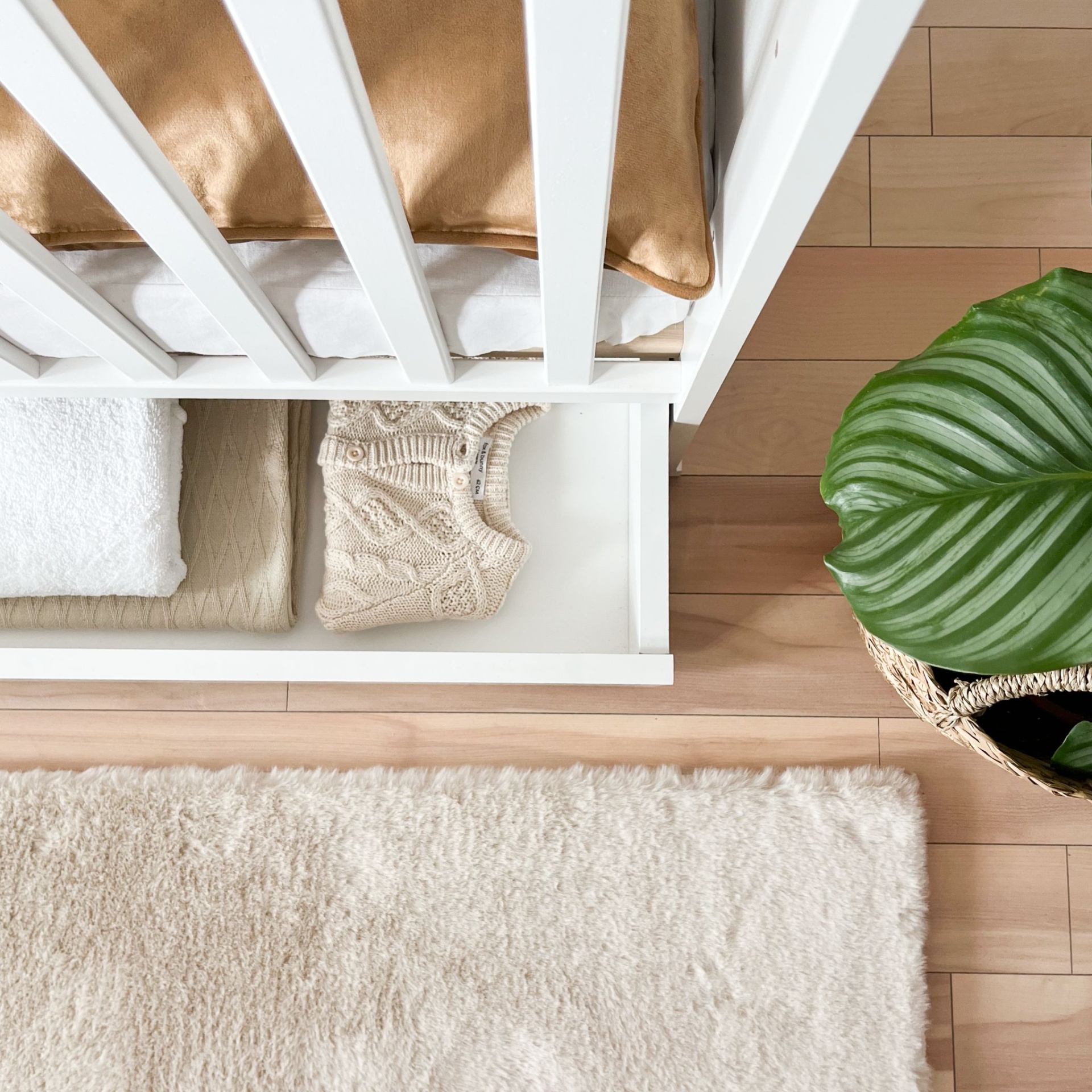 Berço de Bebé PEQUENO CORAÇÃO com Gaveta Berço branco com gaveta aberta contendo roupas e planta verde ao lado