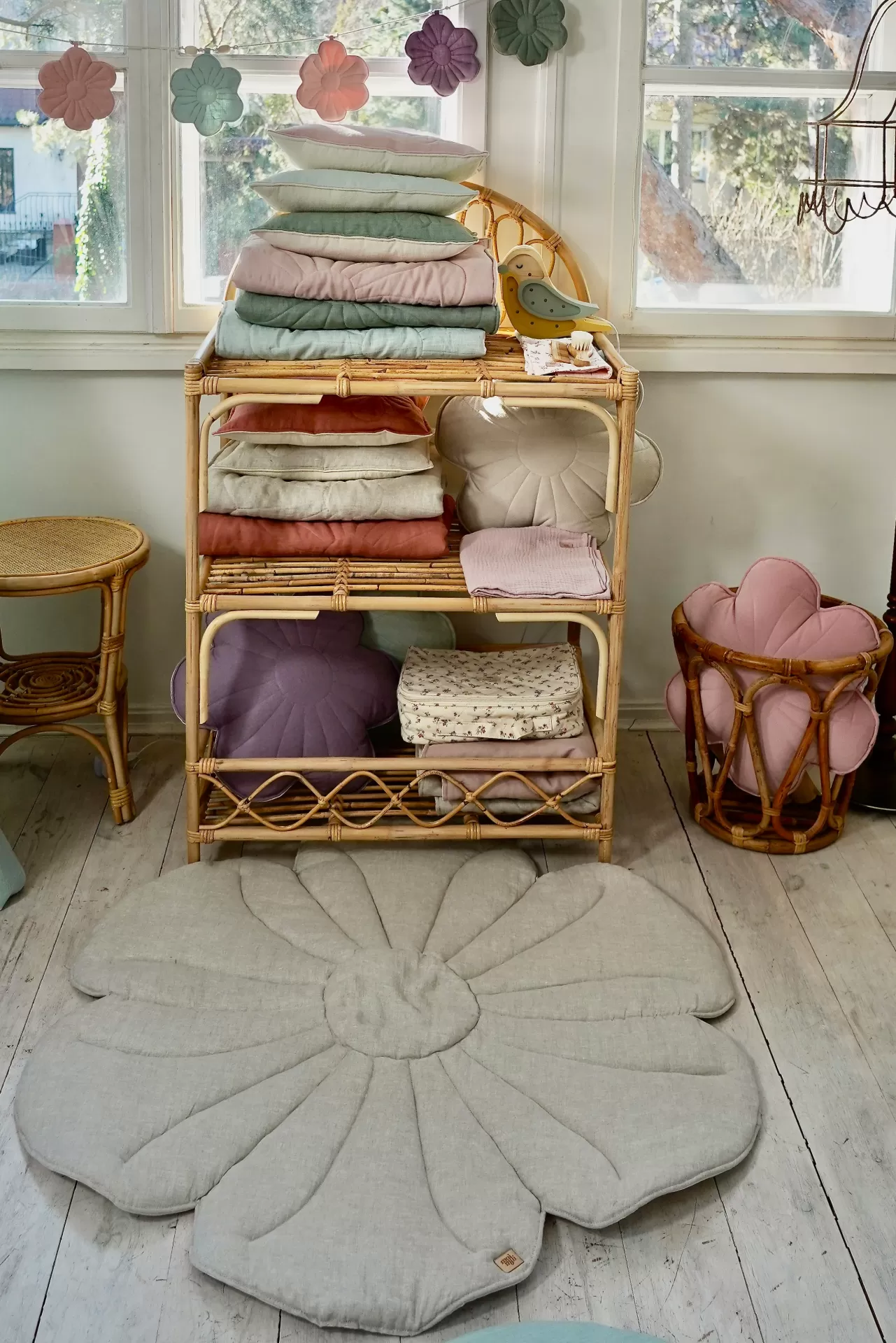 Tapete de Veludo FLOR Estante de vime com almofadas e mantas coloridas, tapete floral cinza no chão e decoração de flores na janela