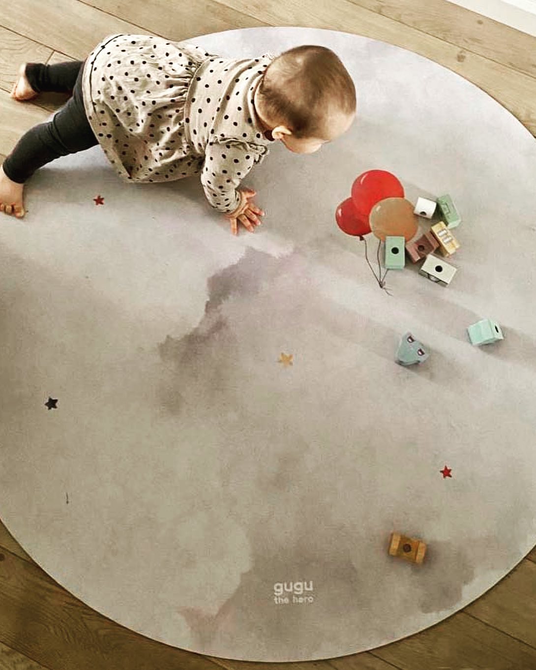 Tapete Redondo de Borracha Natural Balões PRIME Tapete redondo cinza com padrão de nuvens e estrelas coloridas, bebé a rastejar e brinquedos de madeira