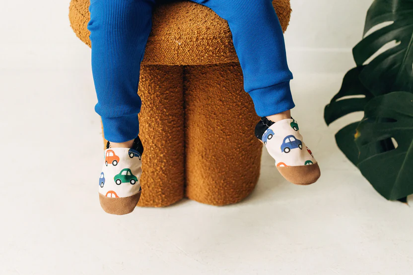 Pés de bebé com meias estampadas de carros sentado numa cadeira castanha texturada