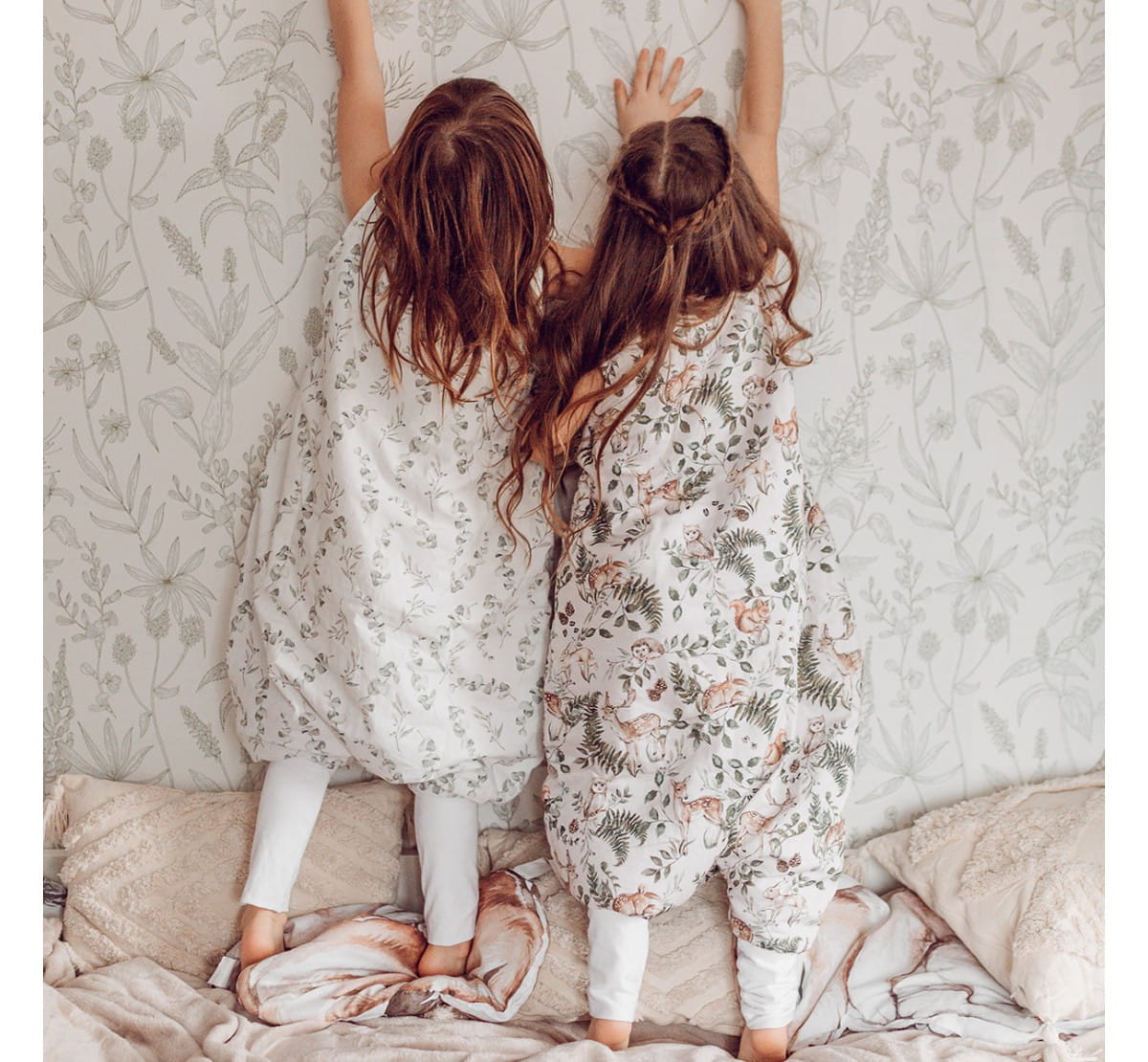 Saco de Dormir com Pernas - Animais da Floresta Bebés com sacos de dormir botânicos numa cama com almofadas claras