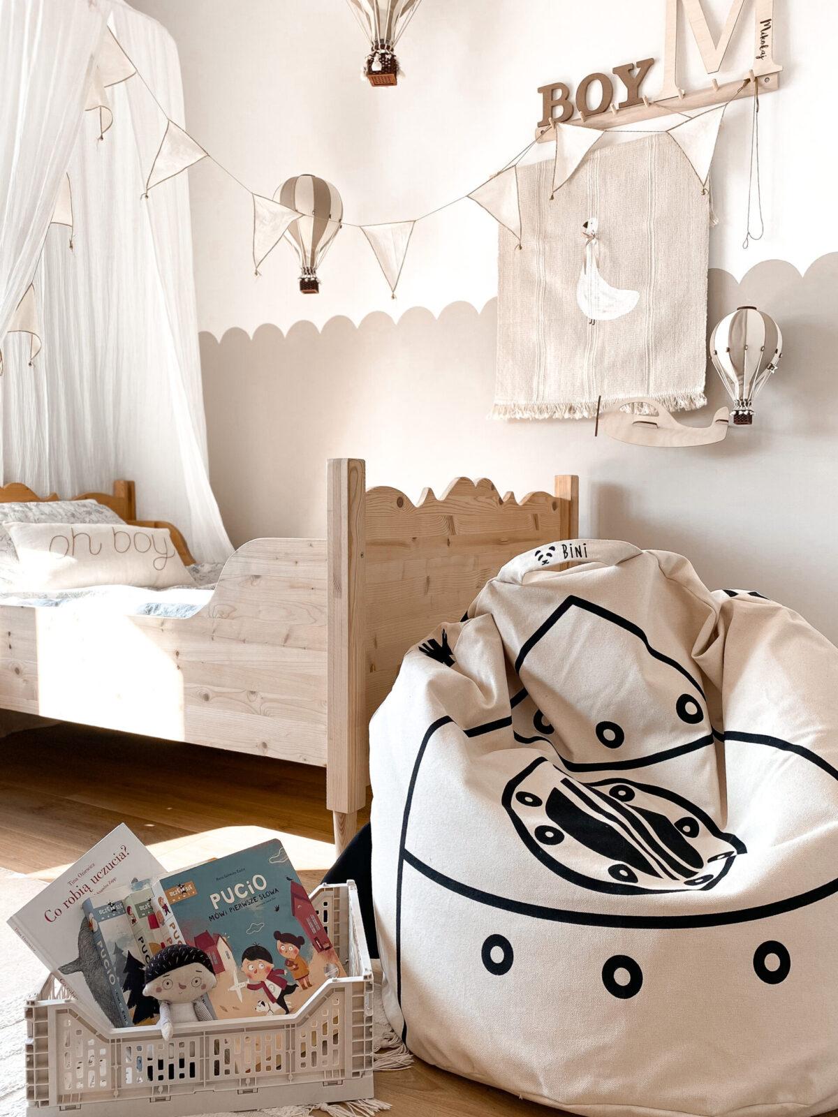 Pufe Bini Grande FOGUETÃO Quarto infantil com cama de madeira clara, pufe estampado, cesta com livros e decoração de balões de ar quente