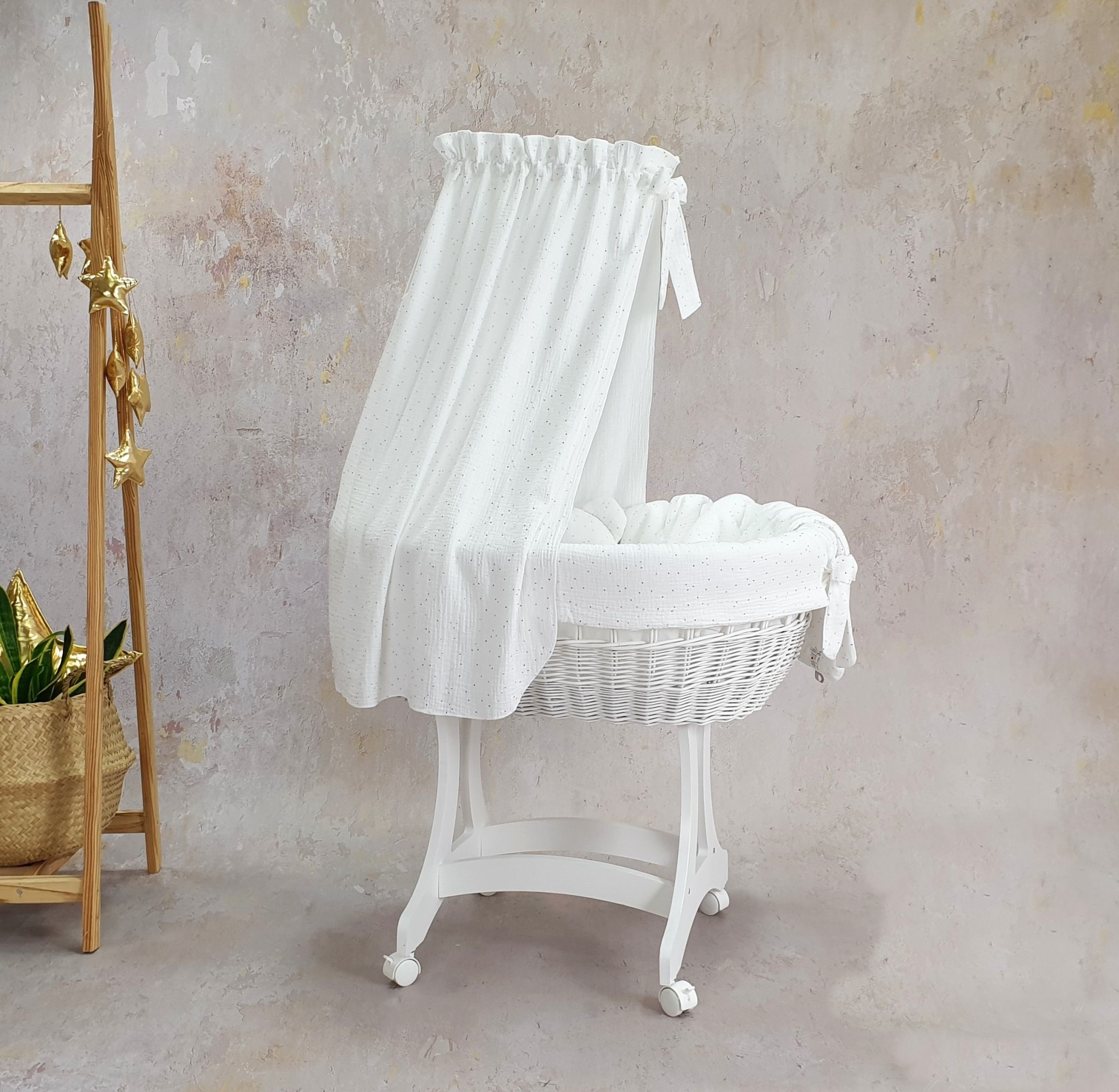 Cesta Moisés de Vime Branco EMMA com Roupa de Cama Berço infantil em vime branco com tecido branco e estrutura em madeira ao lado de escada de madeira com plantas