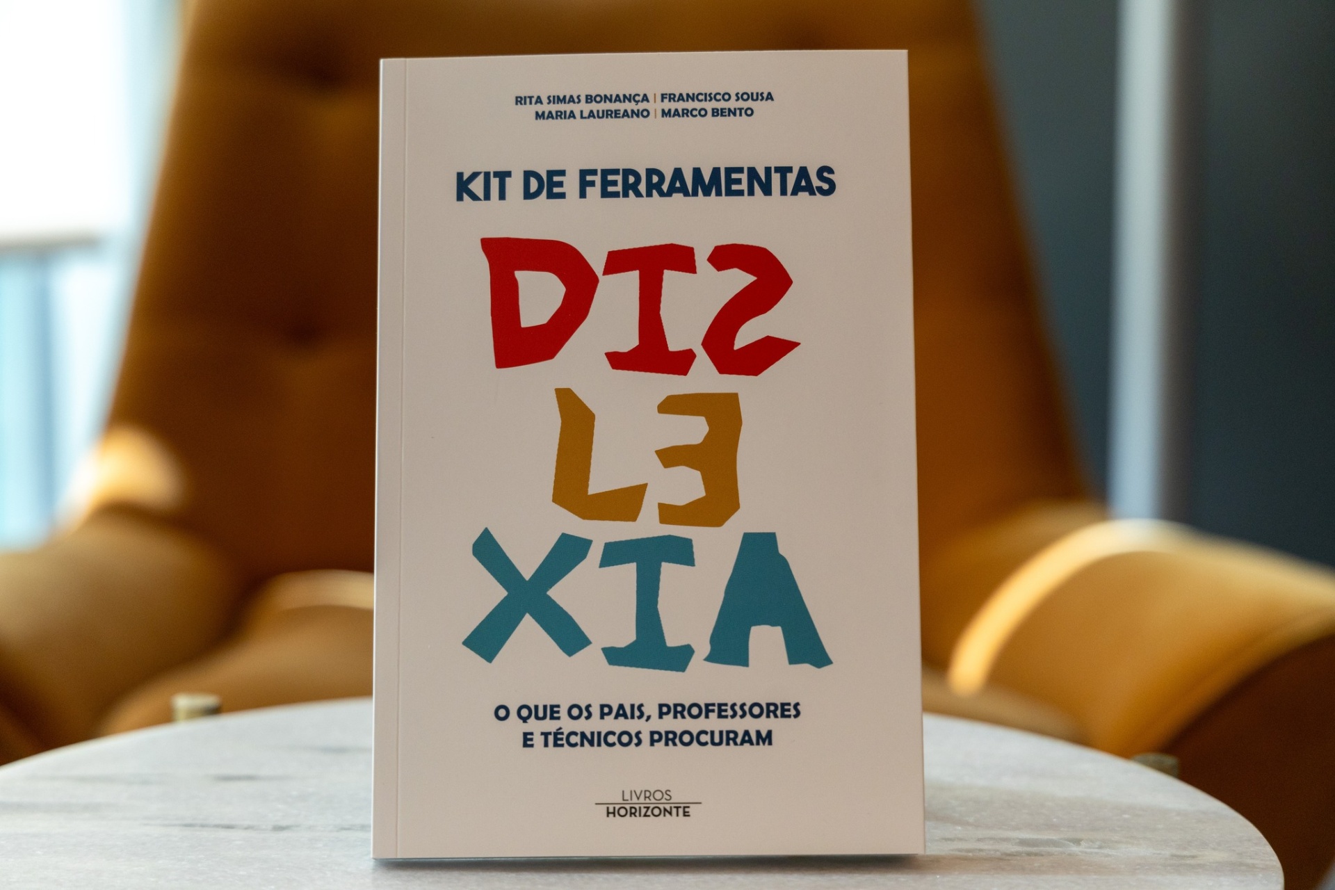 Livro KIT DE FERRAMENTAS DISTÁXIA com capa branca em mesa cinzenta e poltrona castanha ao fundo