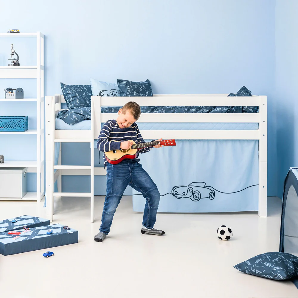 Conjunto de Edredão e Fronha Infantil – Carro Cama alta branca infantil com roupa de cama azul e desenhos de carros, criança tocando guitarra, estante branca ao lado