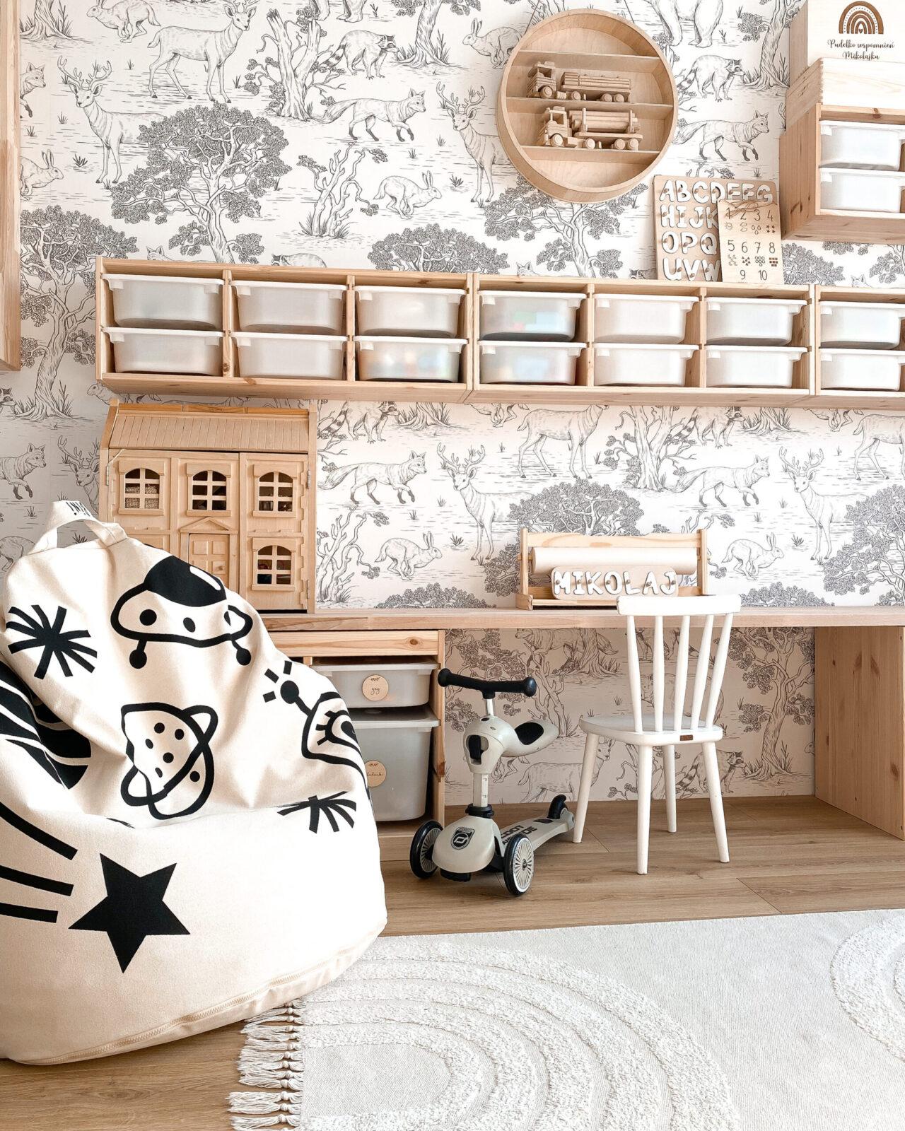 Pufe Bini Grande FOGUETÃO Quarto infantil com prateleiras de madeira, caixas transparentes, papel de parede com animais, puff com estampas pretas, cadeira branca, tapete branco, mini bicicleta e casinha de madeira.