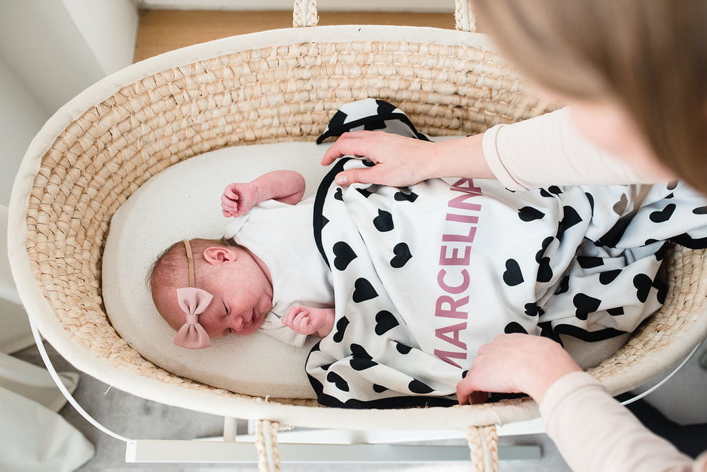 Bebé recém-nascida deitada numa alcofa com manta personalizada e mãe a ajeitar