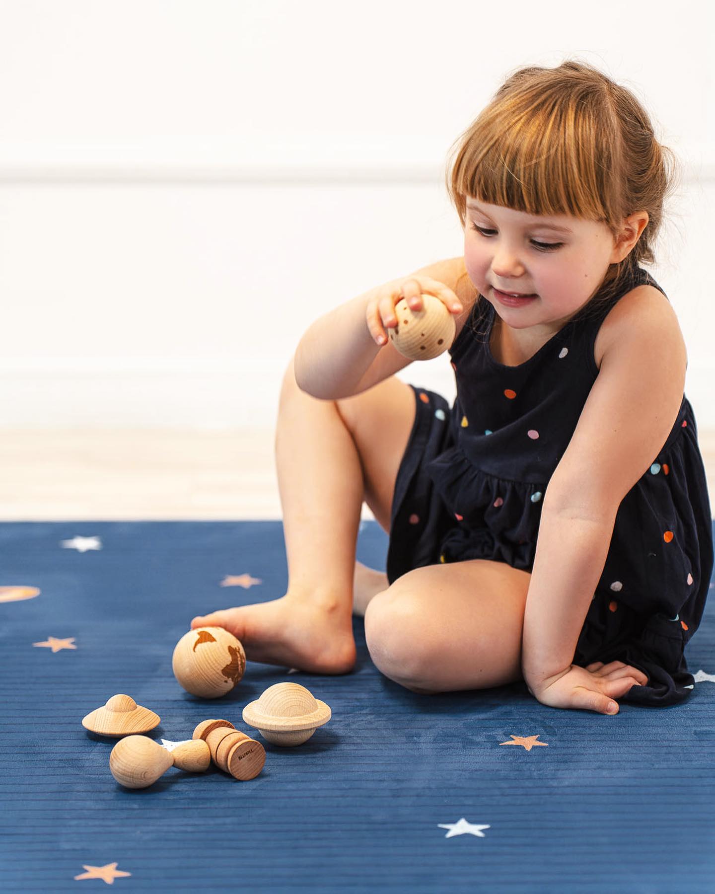 Tapete Grande Borracha Natural GALÁXIA Criança a brincar com brinquedos espaciais de madeira num tapete azul com estrelas