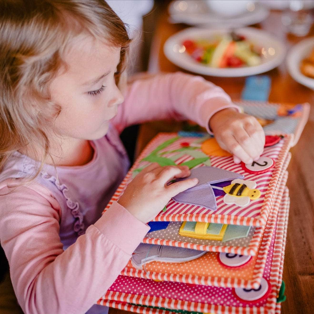 Criança a explorar livro de pano colorido com números e imagens em tecido