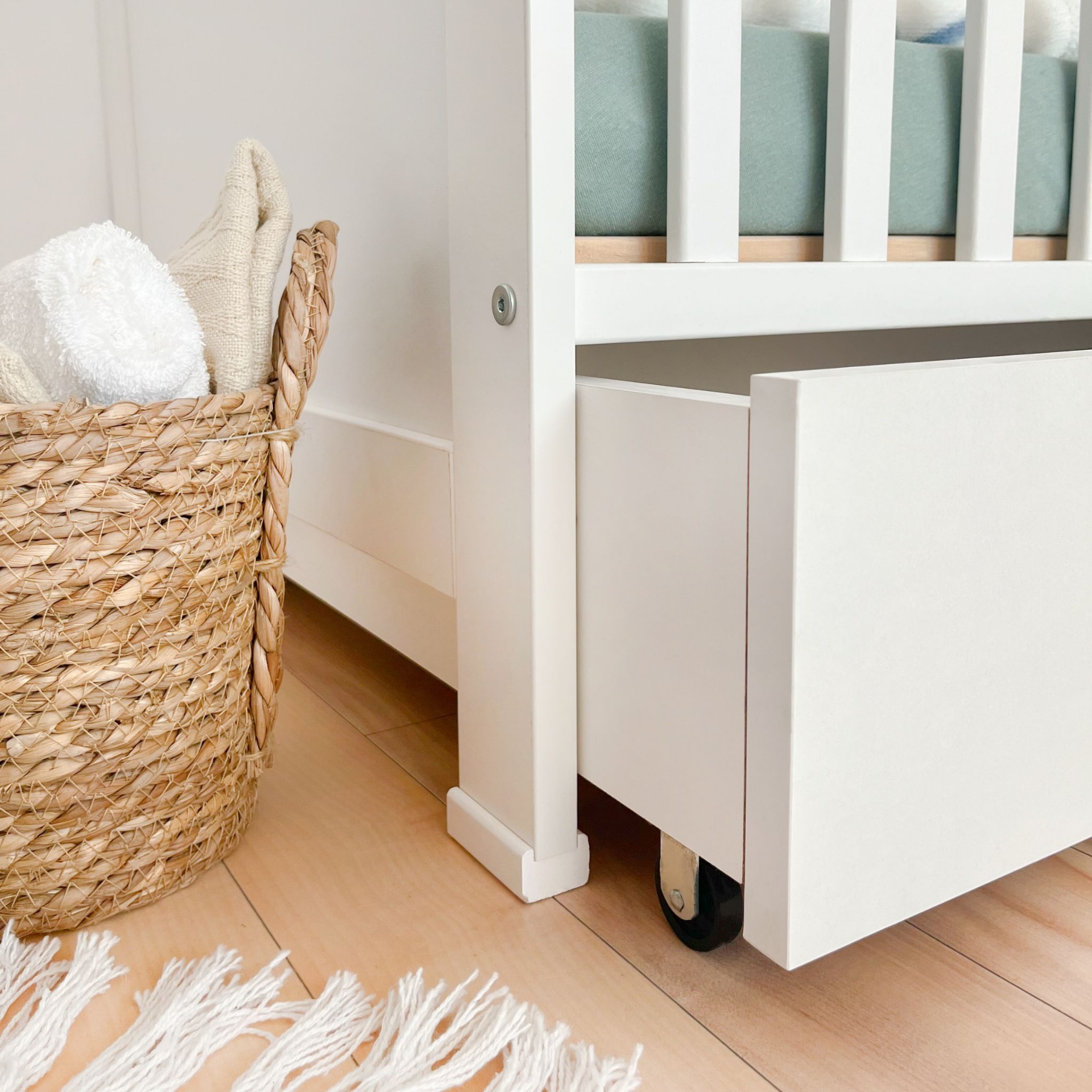 Berço de Bebé PEQUENO CORAÇÃO com Gaveta Cesto tecido bege com toalha branca e tecido creme ao lado de cama branca com gaveta aberta e tapete branco