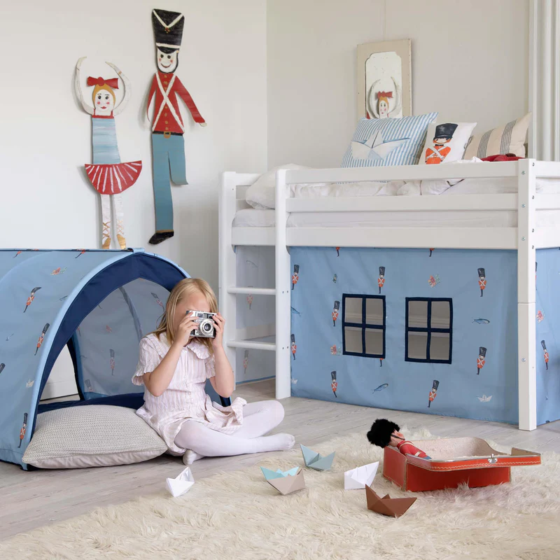 Quarto infantil com cama branca alta e decoração de soldados de chumbo, tenda azul e brinquedos no chão.