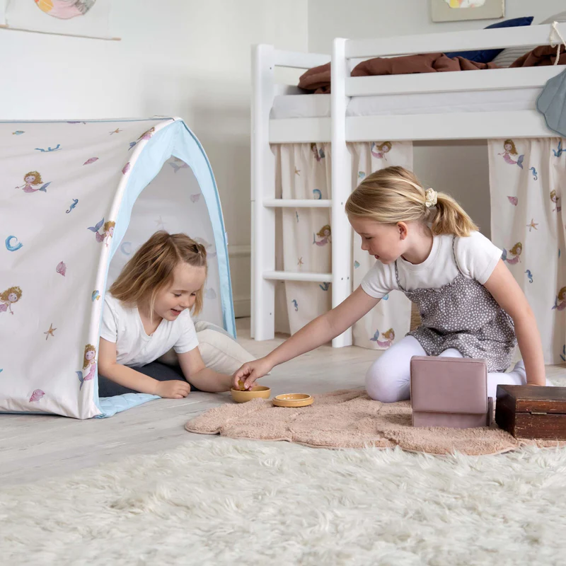 Tenda infantil com padrão de sereias e cama alta branca com cortinas combinando