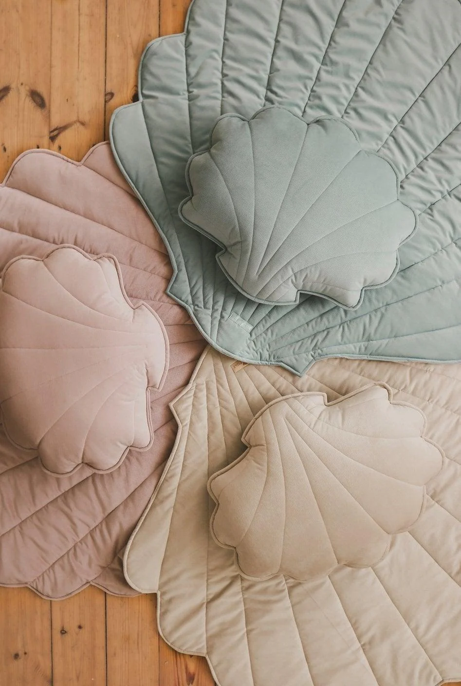 Tapete Veludo CONCHA Almofadas e colchas em forma de concha em tons pastel sobre chão de madeira