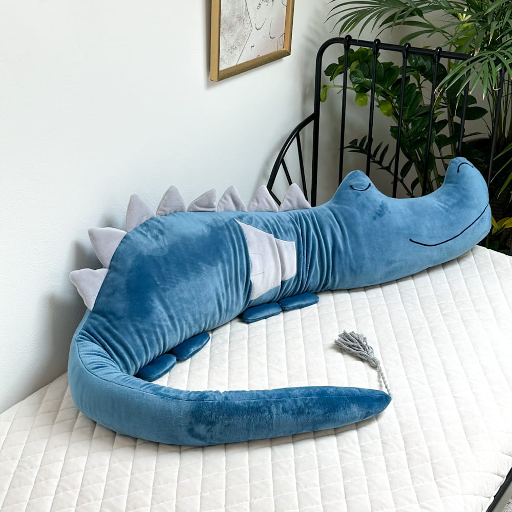 Protetor de Cama/Berço DRAGÃO PELÚCIA Almofada em forma de crocodilo azul numa cama com colchão bege