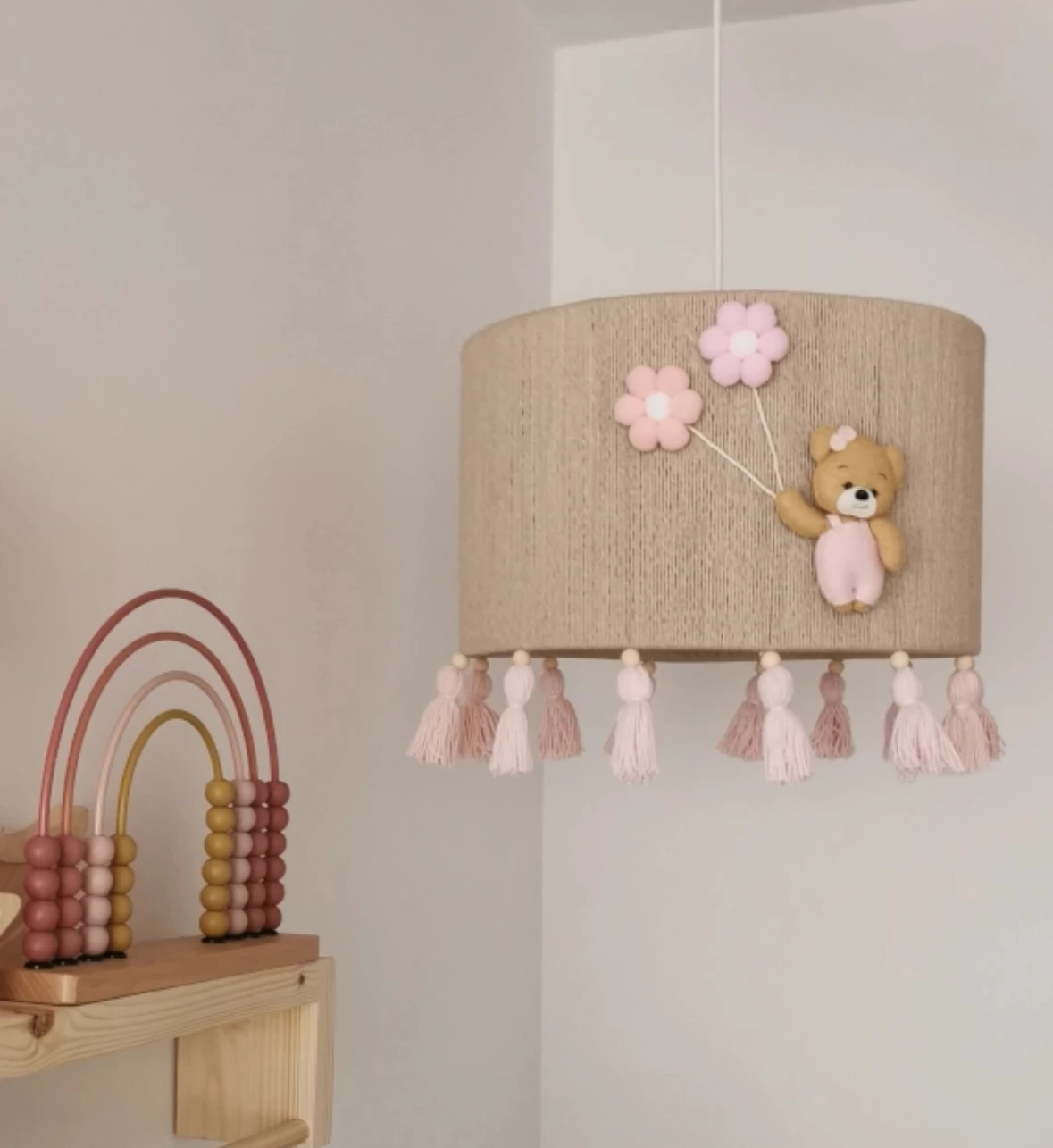 Candeeiro Teto URSO com Balão Flor Rosa Candeeiro de teto redondo com ursinho e balões cor-de-rosa, suspenso num quarto branco com prateleira de madeira e brinquedo colorido.