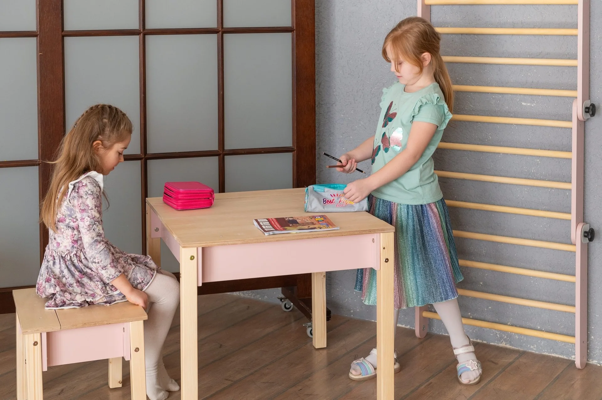 Conjunto de Mesa e Cadeira Infantil com Arrumação Conjunto de mesa e bancos infantis em madeira clara com dois estojos coloridos sobre a mesa