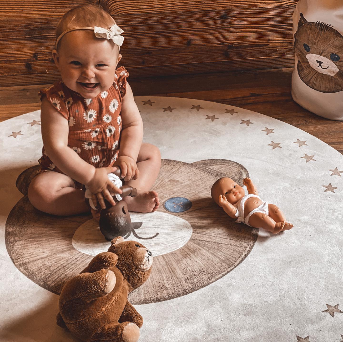 Tapete Redondo Borracha Natural URSO TEDDY Bebé sentada num tapete redondo com padrão de urso, com três brinquedos ao seu redor.