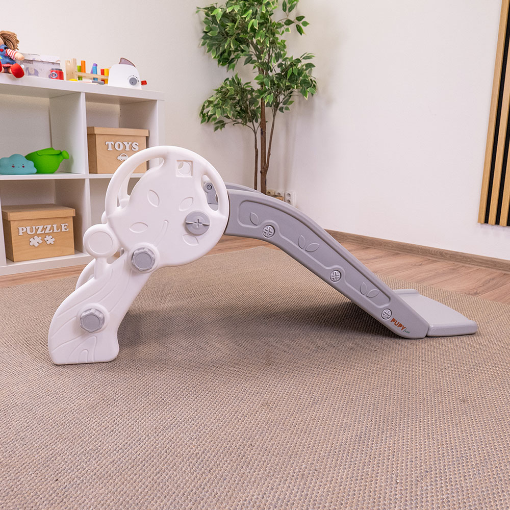 Escorrega Infantil PUPY Para Interior e Exterior Escorrega infantil cinzento claro e branco em sala com estante e planta