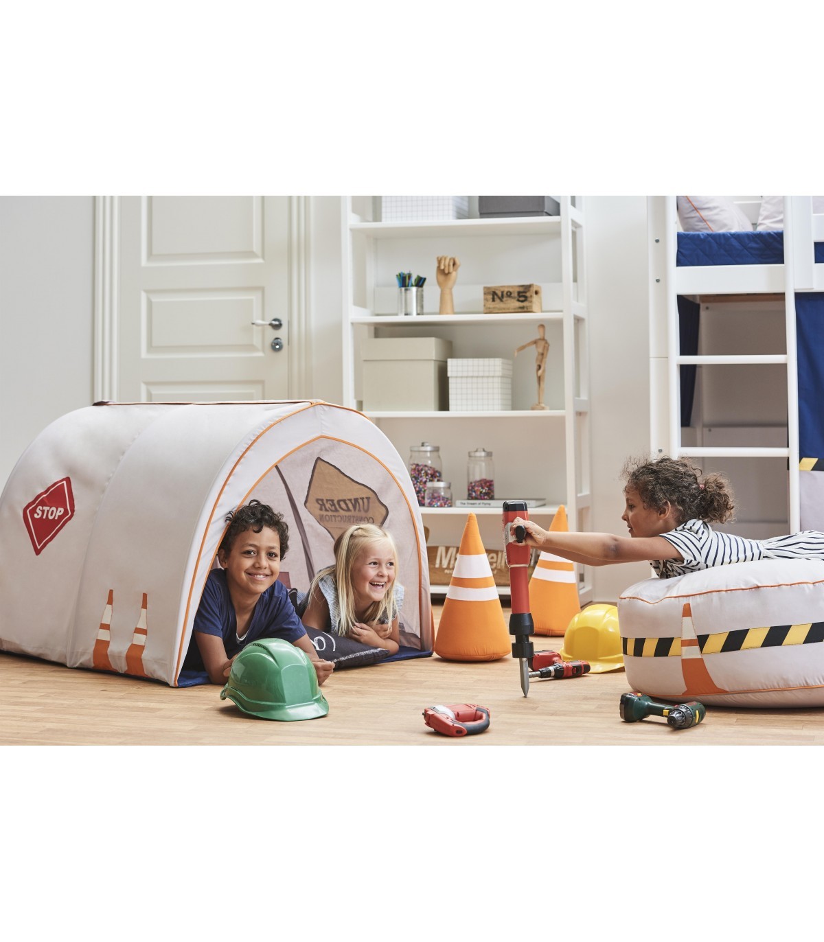 Túnel de Brincar - Construção Crianças a brincar num túnel de brincadeira temático de construção com acessórios como cones, capacetes e ferramentas douradas.