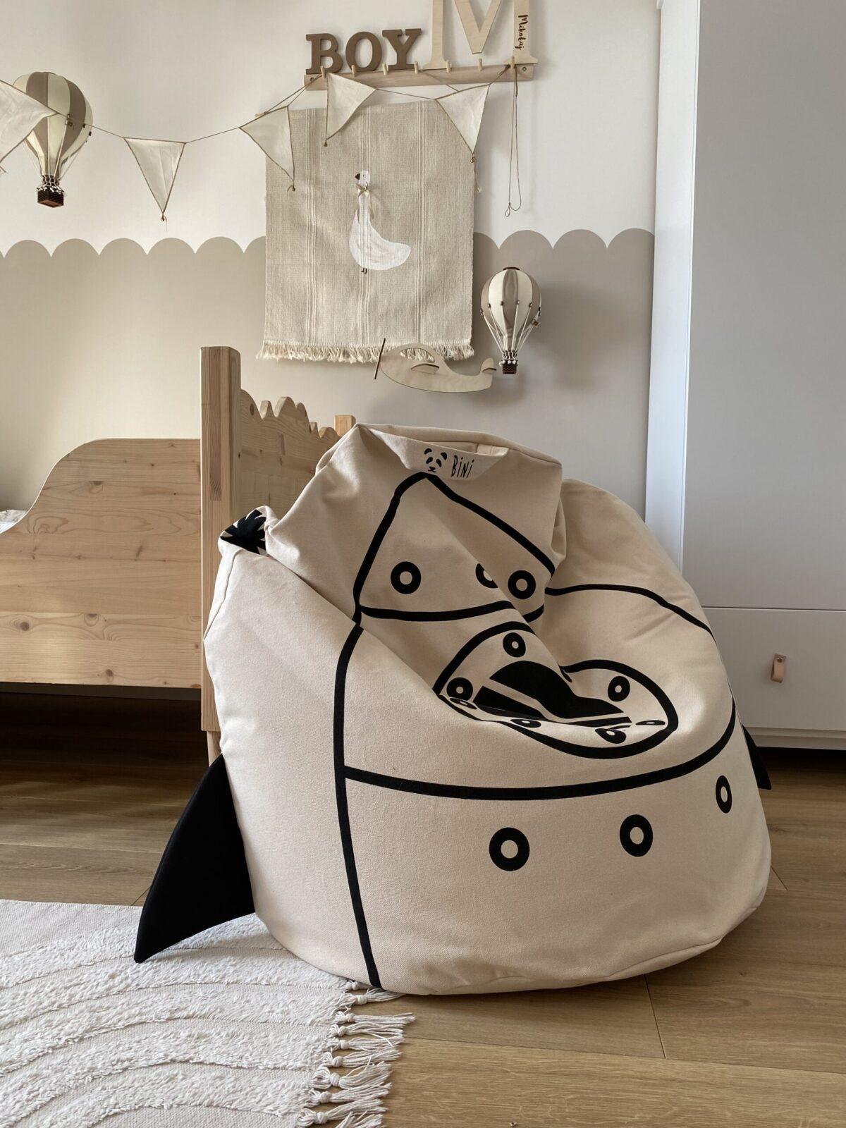 Pufe Bini Grande FOGUETÃO Pufe infantil em tecido bege com desenho de tubarão preto num quarto infantil com decoração neutra