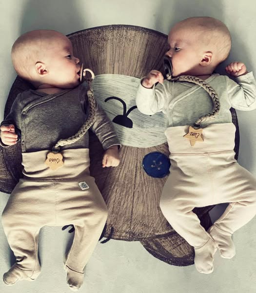Tapete Redondo Borracha Natural URSO TEDDY Dois bebés vestidos com macacões e babetes de algodão de cores neutras deitados num tapete com imagem de urso.
