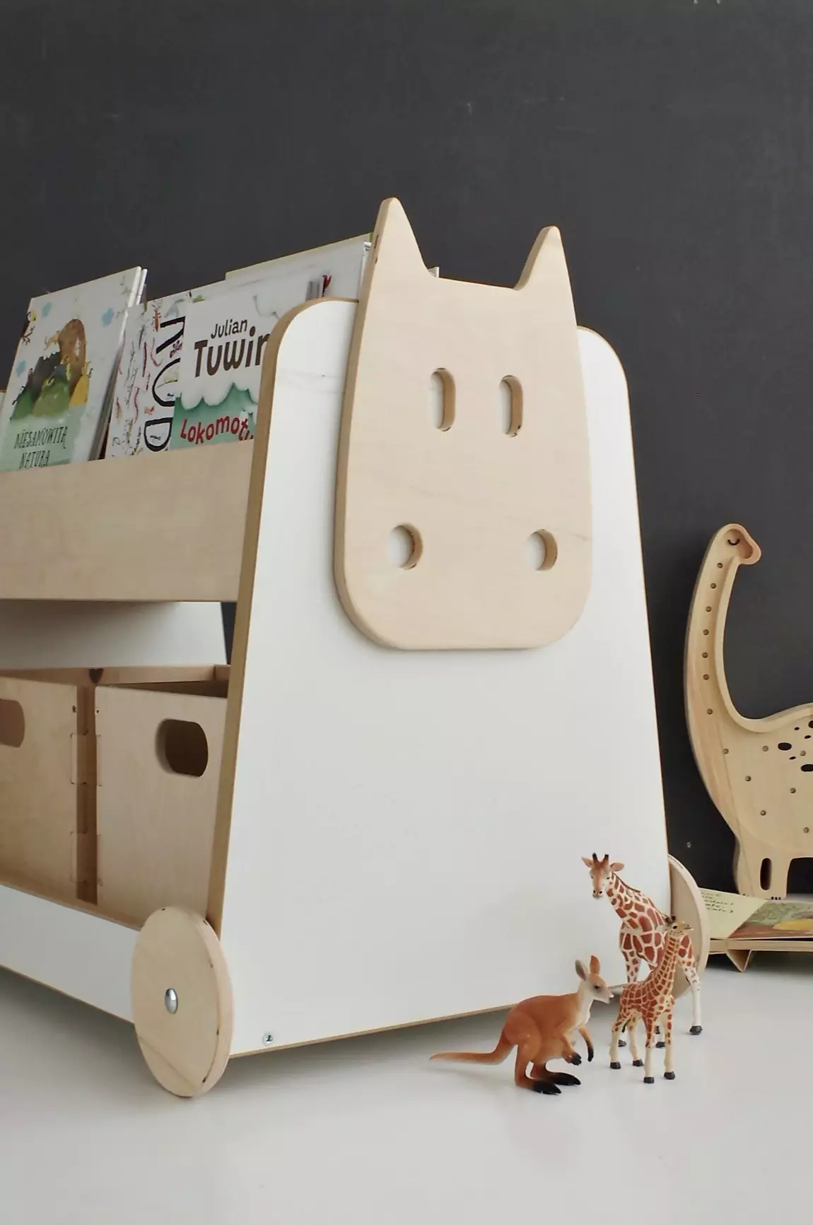 Estante de Madeira Sobre Rodas Cesto organizador de brinquedos de madeira com decoração de rosto de vaca e brinquedos animais em frente.